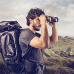 young explorer in high mountain looks horizon with binoculars