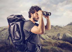 young explorer in high mountain looks horizon with binoculars